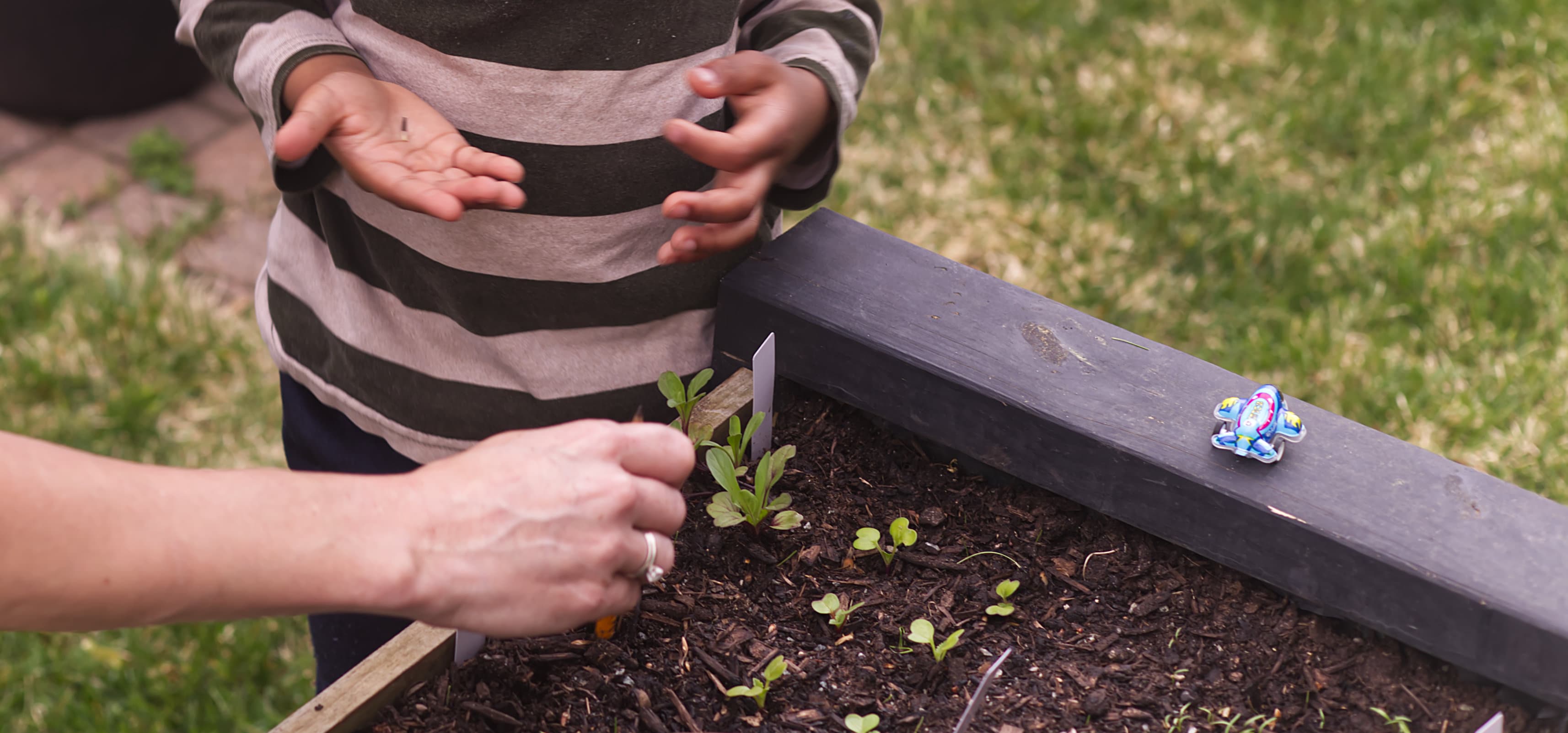 Child Tending Raised Garden Bed — Mission Feature A child exploring and tending a raised planter box garden, hands engaged with the plants.